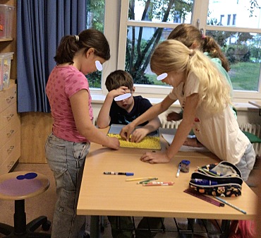 Hier sind Kinder zu sehen, die zusammen eine Aufgabe am Tisch bearbeiten.